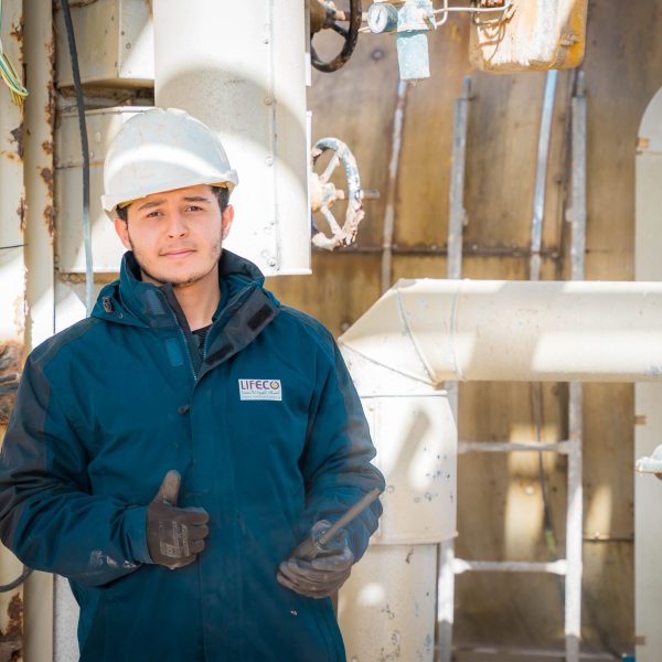 Engineer in safety gear within an industrial setting in Libya, pipes and machinery visible.