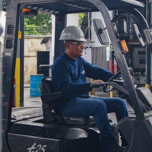 An industrial worker wearing protective gear operates a forklift inside a warehouse.